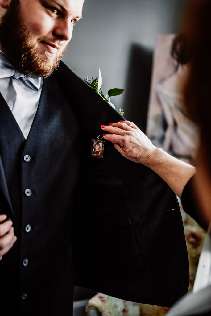 a groom and his aunt celebrating his mom with a pendant inside his jacket on his wedding day