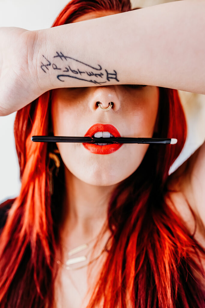 close up of a make up artist holding a small make up brush in her mouth